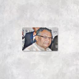 A close-up photograph of an older Indian man with glasses and gray hair