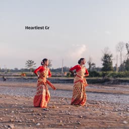 Two women performing traditional Bihu dance in traditional Mekhela Sador by a riverbank.