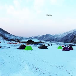 A scenic view of a campsite covered in deep snow surrounded by high mountain peaks at dusk.