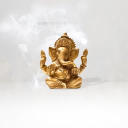A metallic gold Lord Ganesha statue sitting in a meditative pose against a white smoky background.