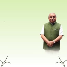 A smiling middle-aged Indian man wearing a traditional green Nehru jacket and white shirt against a pale green gradient background.