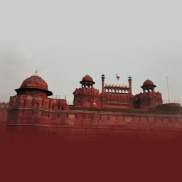 The iconic Red Fort in Delhi, India, with its prominent red sandstone walls and turrets under a pale sky.