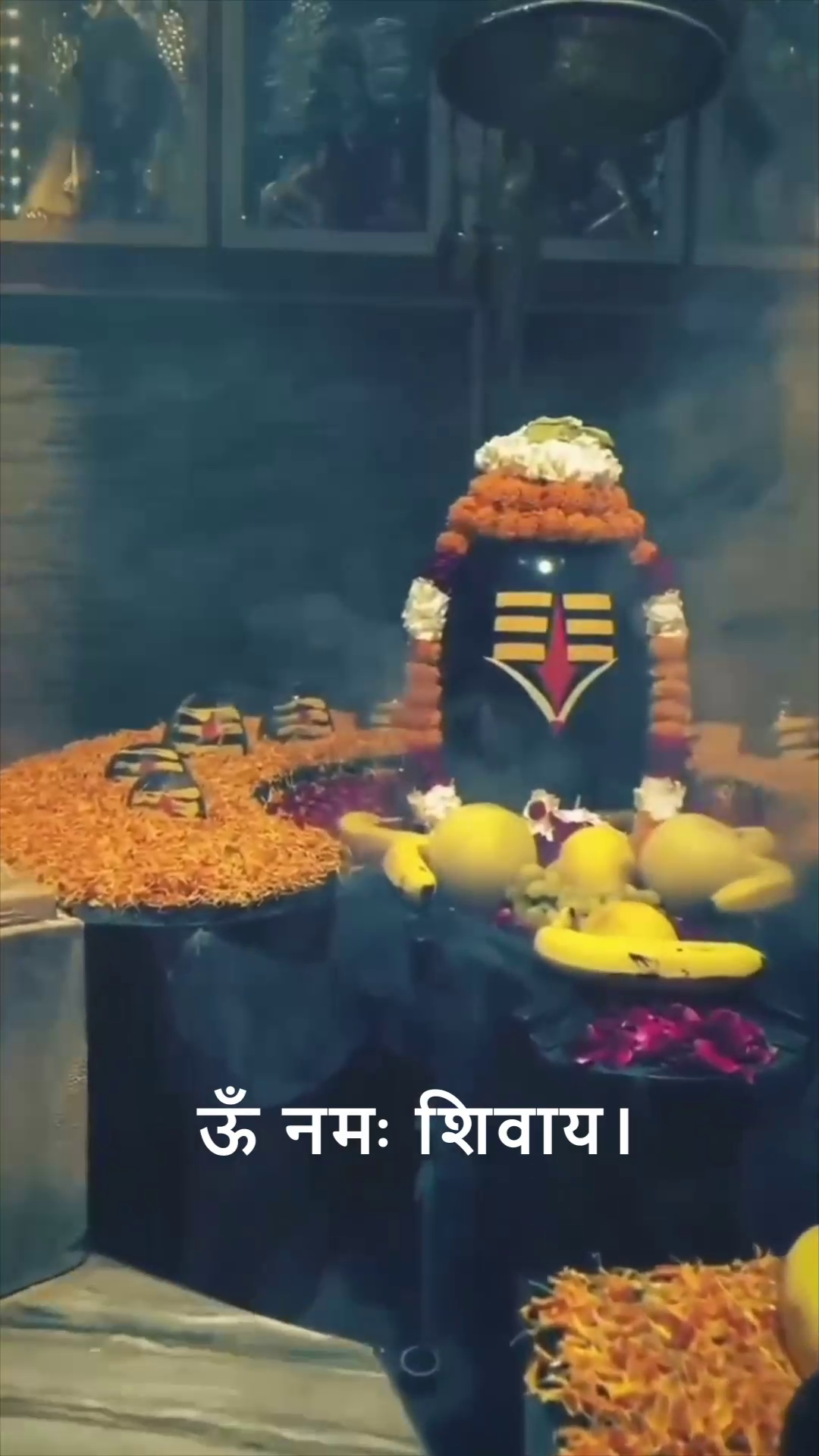A beautiful Shiva Lingam adorned with marigold flowers and fruits with the text Om Namah Shivaya written in Hindi