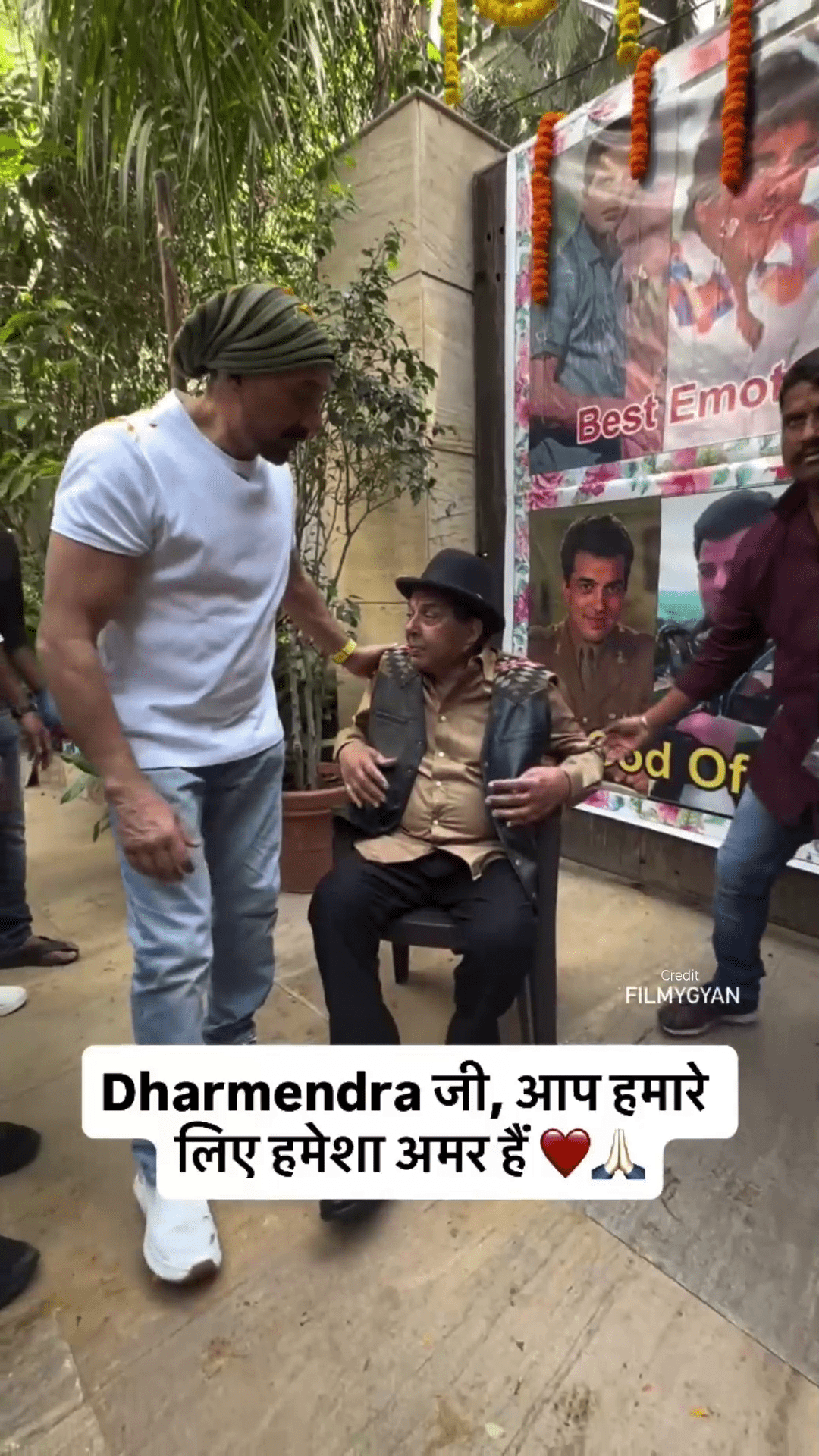 Sunny Deol standing next to his father Dharmendra who is sitting on a chair