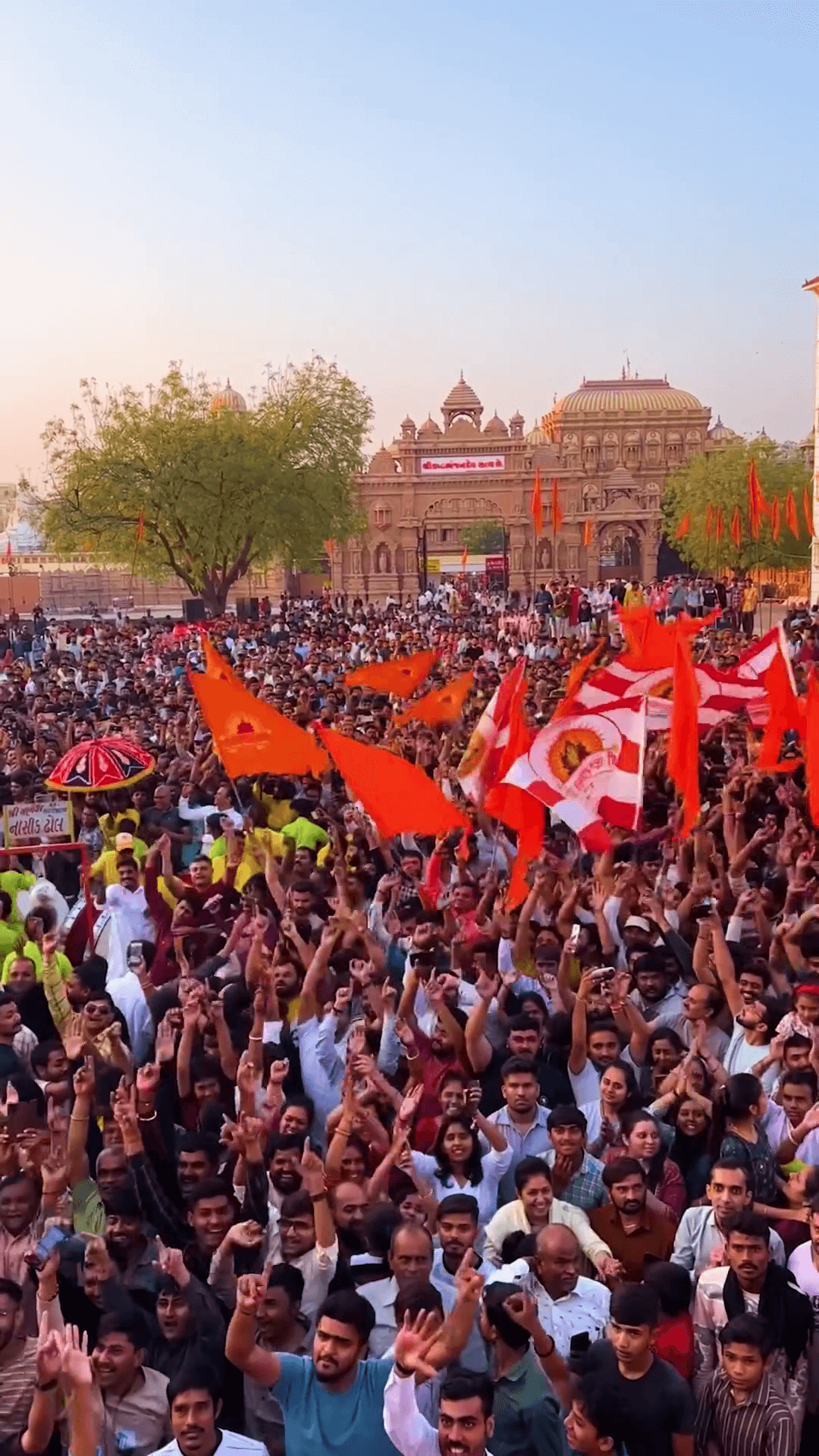 A large crowd of people celebrating with orange flags in front of an Indian temple