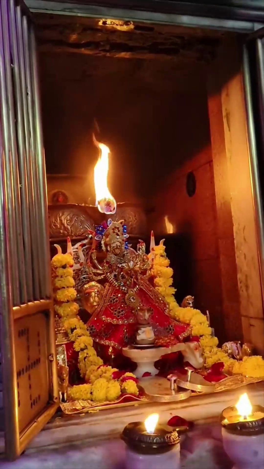 A beautiful idol of Goddess Durga adorned with flowers and glowing with a flame above her head inside a temple sanctuary.