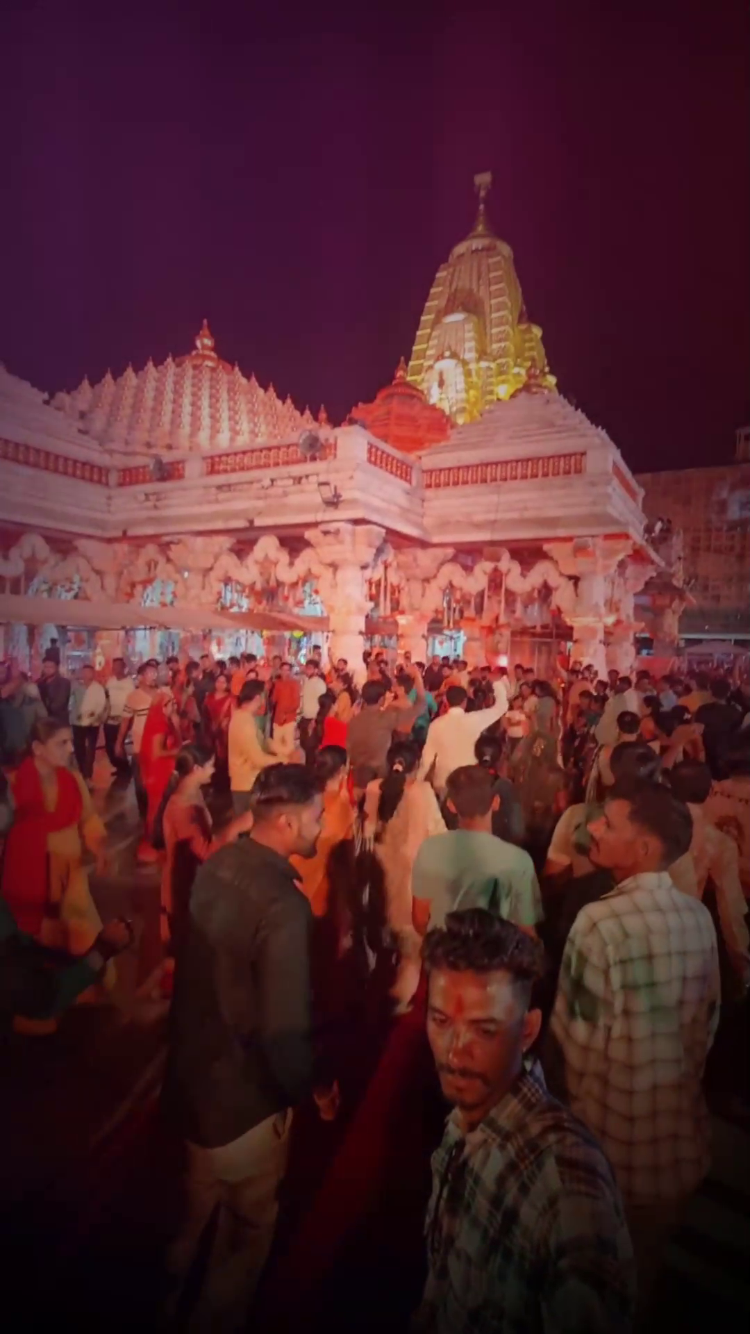 A large crowd of devotees gathered at a brightly lit Hindu temple during the evening hours