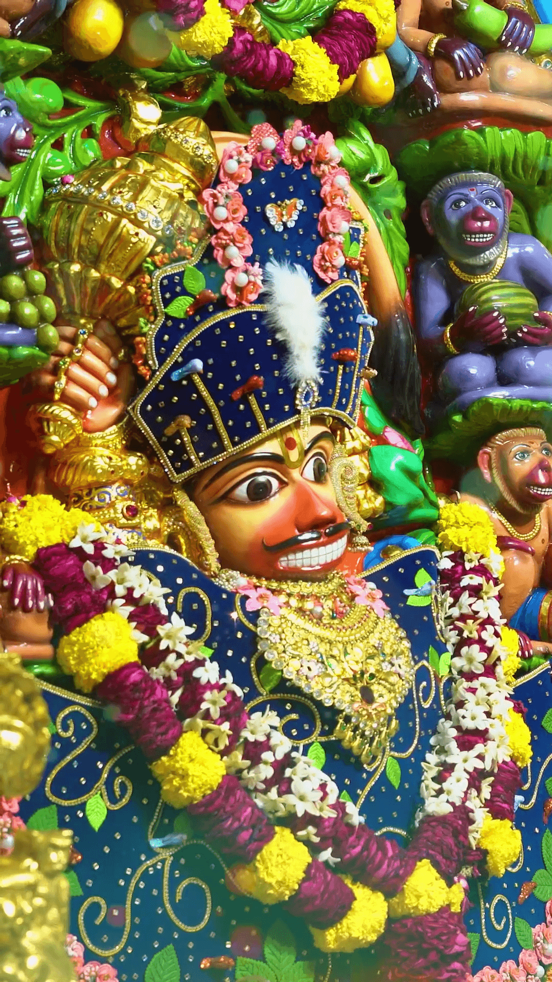 A brightly decorated Hindu deity idol adorned with floral garlands, gold jewelry, and a crown
