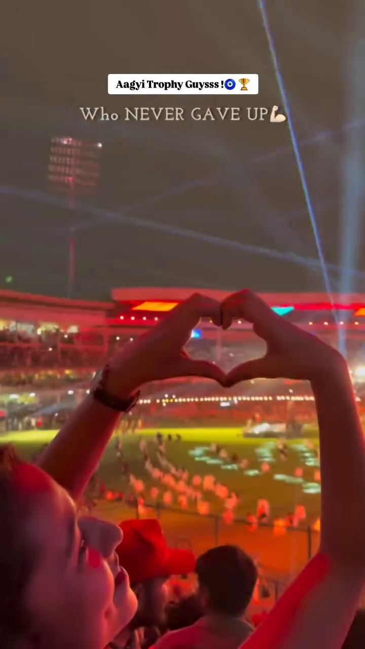 A fan making a heart shape with hands at a stadium during a night cricket match victory celebration