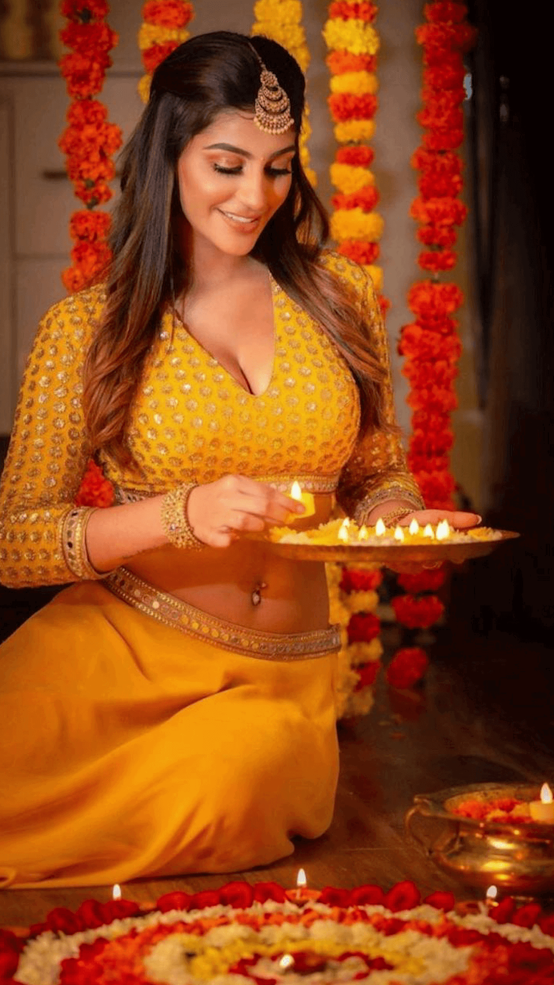 A beautiful woman in a traditional yellow lehenga holding a lit diya during Diwali celebrations