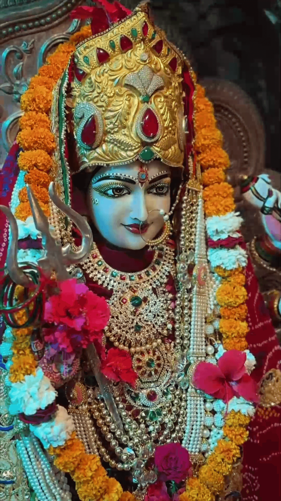 A beautifully decorated statue of Goddess Durga featuring intricate gold jewelry, flowers, and a trident.