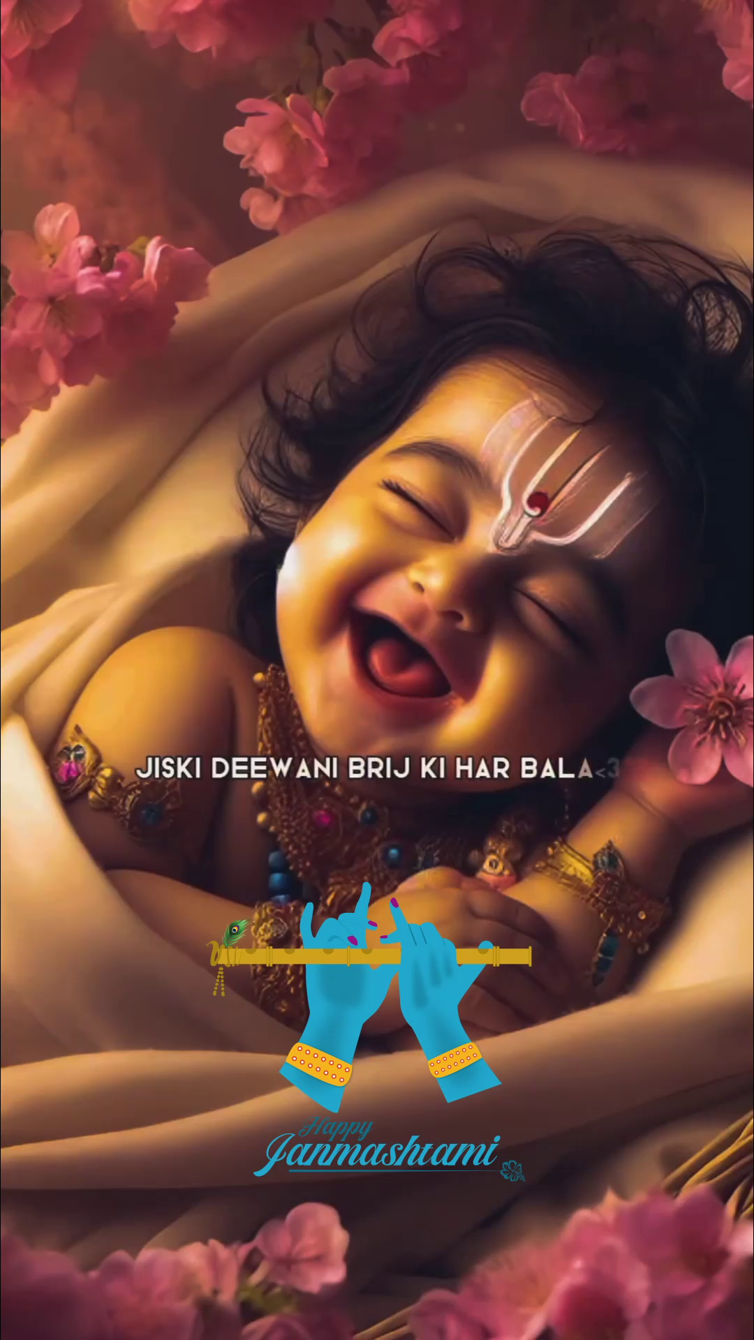 A smiling baby representing Lord Krishna, decorated with a tilak, surrounded by pink flowers with a flute graphic and Happy Janmashtami text.