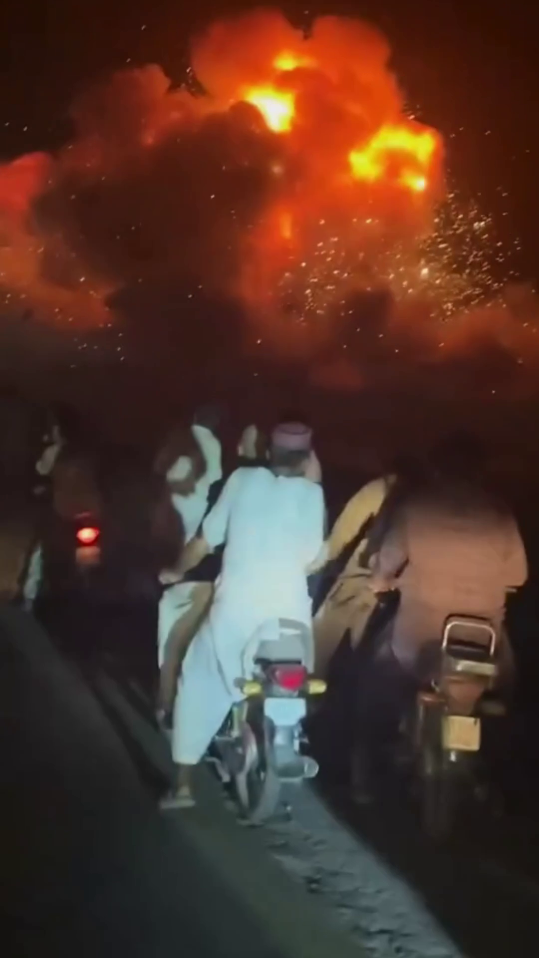 Motorcyclists riding on a dark road beneath a large, glowing orange explosion in the night sky