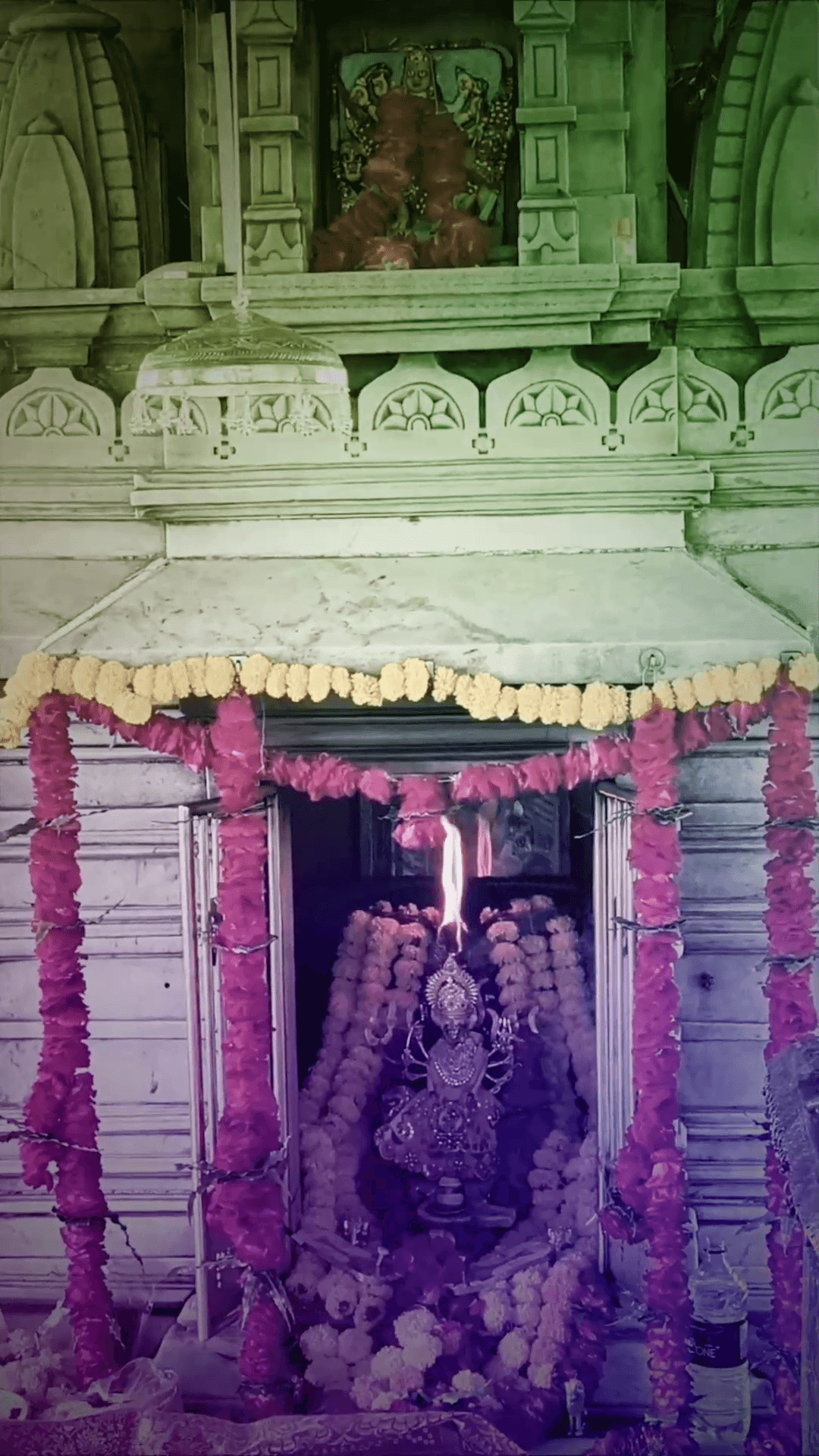 A sacred Hindu temple shrine adorned with vibrant pink and yellow flower garlands featuring a central idol with a flame.