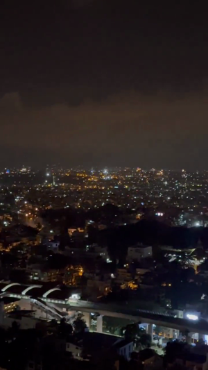 A panoramic aerial view of a city landscape at night with illuminated streets and buildings under a dark sky.