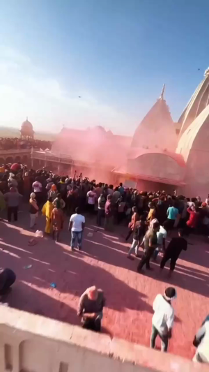 A crowd of people celebrating Holi in front of the Banke Bihari temple in Vrindavan, India, with pink powder in the air.