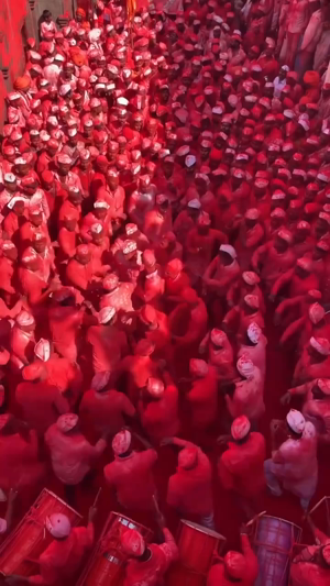 A large crowd of people covered in red Holi powder celebrating at a festival