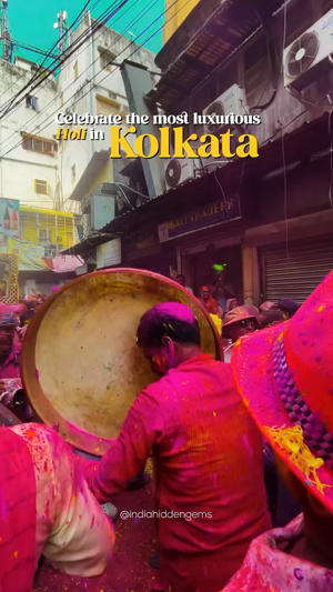 Person playing a large drum during a vibrant Holi festival in the streets of Kolkata.