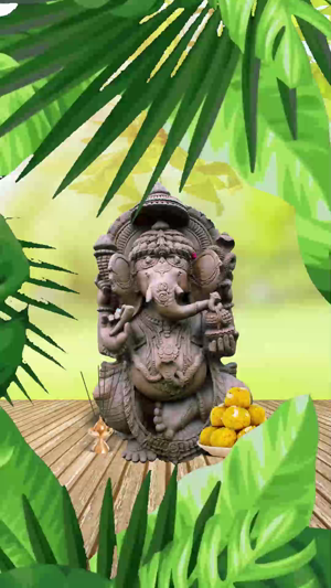 A stone statue of Lord Ganesha positioned on a wooden platform surrounded by tropical green leaves, with a plate of yellow modak sweets.