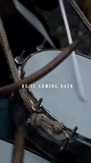 A close-up shot of a drum being played with the text 'HE IS COMING BACK' overlaid.